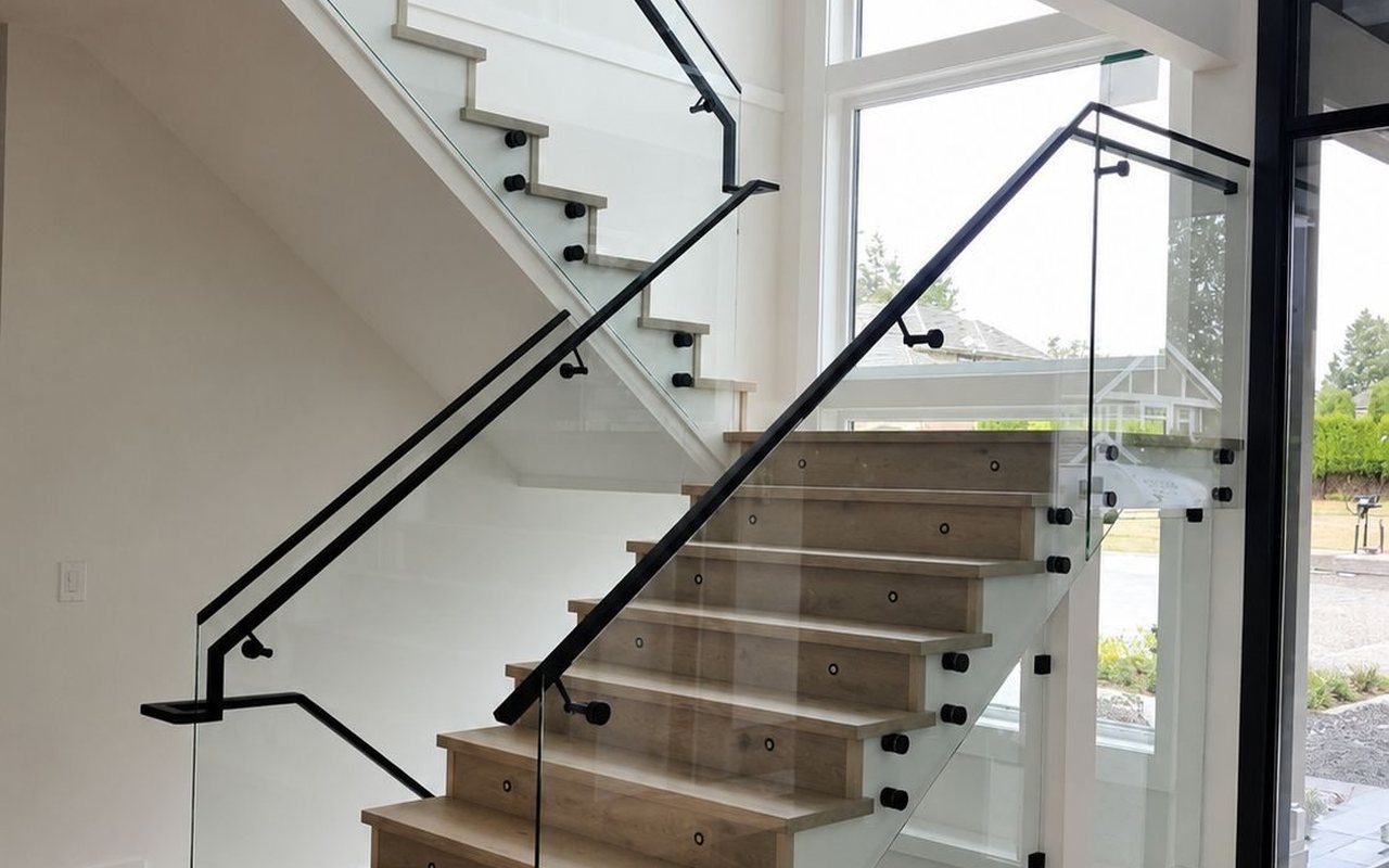 Finished staircase with frameless glass railing and matte black handrail by HJR Construction